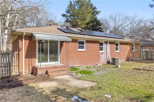 rear view of property featuring entry steps, fence, central air condition unit, roof mounted solar panels, and brick siding