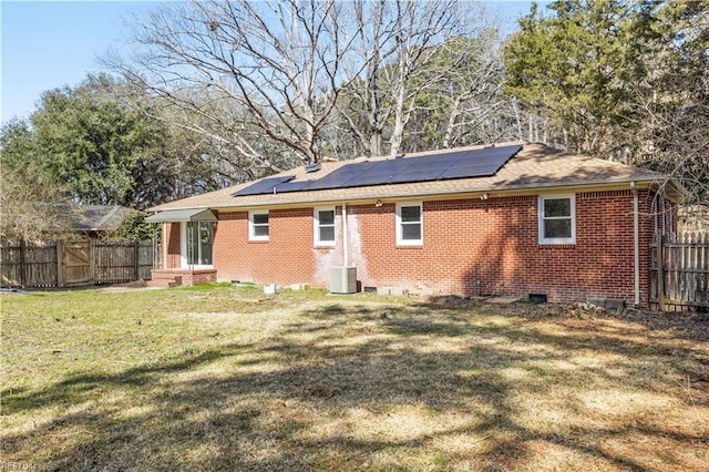 back of house with brick siding, a yard, roof mounted solar panels, fence, and cooling unit