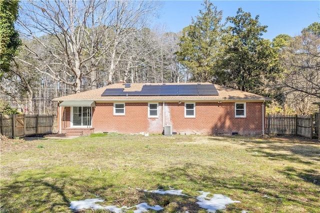 rear view of property featuring entry steps, a fenced backyard, crawl space, roof mounted solar panels, and brick siding