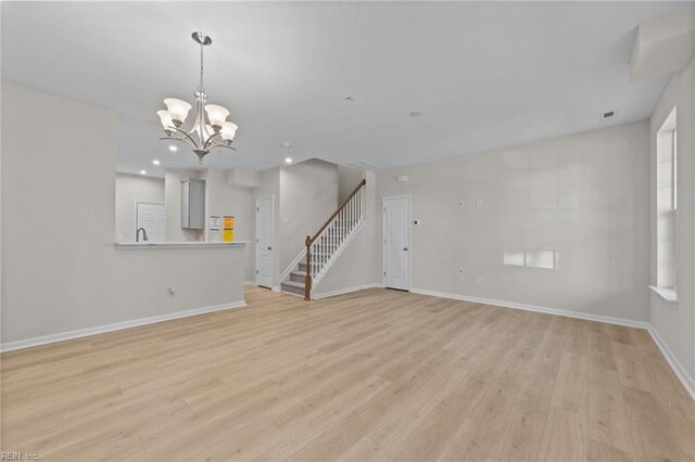 unfurnished living room featuring light wood-type flooring, an inviting chandelier, baseboards, and stairway