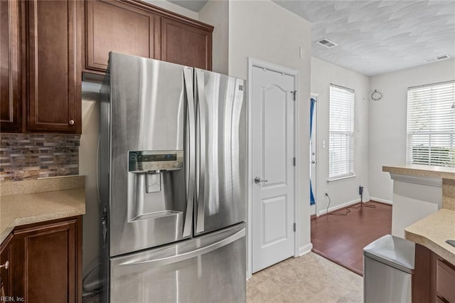 kitchen featuring stainless steel fridge, visible vents, light countertops, and decorative backsplash