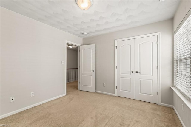 unfurnished bedroom with a closet, light carpet, and baseboards