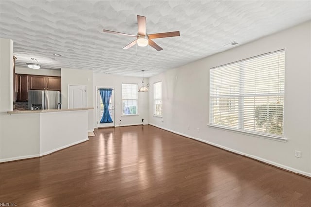 unfurnished living room with baseboards, visible vents, a ceiling fan, dark wood-style floors, and a textured ceiling