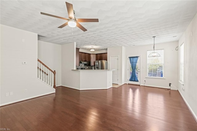 unfurnished living room featuring a textured ceiling, wood finished floors, a ceiling fan, baseboards, and stairs