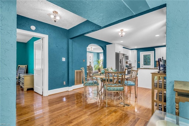 dining space with arched walkways, a textured wall, light wood finished floors, and visible vents