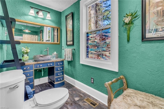 bathroom with toilet, vanity, visible vents, and a textured wall