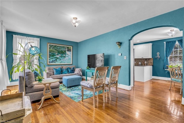 living room with arched walkways, light wood-type flooring, baseboards, and plenty of natural light