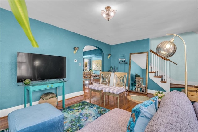 living area featuring arched walkways, stairway, wood finished floors, and baseboards