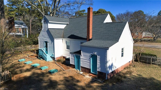 rear view of property featuring a shingled roof, a chimney, and fence