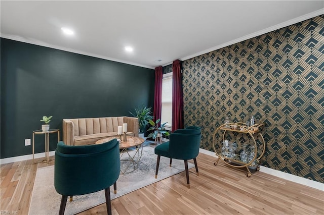 sitting room with crown molding, an accent wall, and wallpapered walls