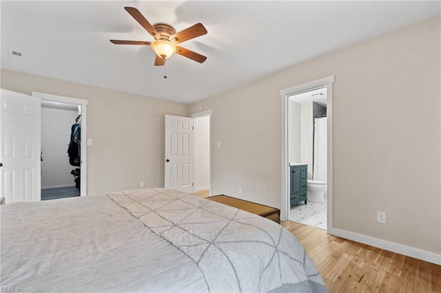 bedroom featuring light wood finished floors, baseboards, a ceiling fan, connected bathroom, and a walk in closet