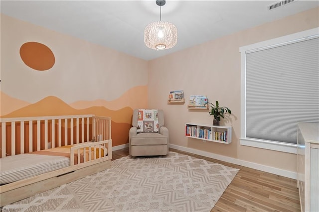 bedroom with a nursery area, baseboards, visible vents, and wood finished floors