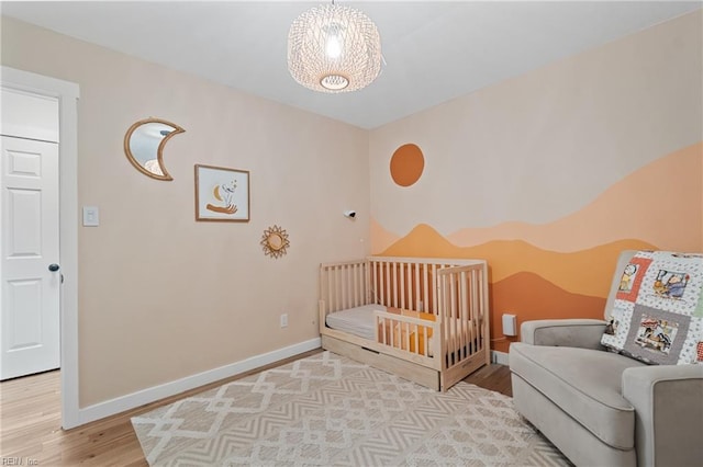 bedroom featuring a crib, baseboards, and wood finished floors