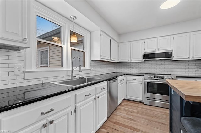 kitchen with pendant lighting, appliances with stainless steel finishes, white cabinetry, a sink, and light wood-type flooring