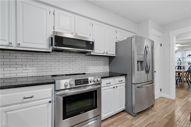 kitchen featuring light wood finished floors, dark countertops, appliances with stainless steel finishes, white cabinetry, and backsplash