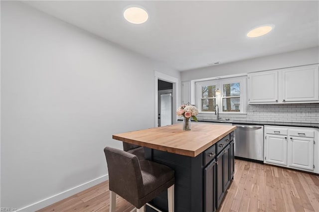 kitchen with stainless steel dishwasher, a breakfast bar area, butcher block countertops, and white cabinetry