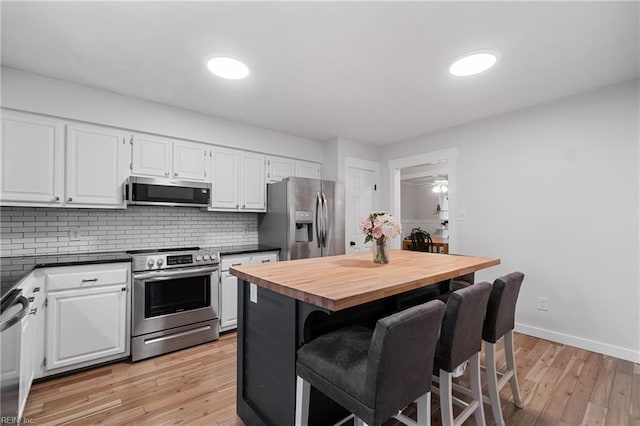 kitchen featuring appliances with stainless steel finishes, white cabinets, decorative backsplash, and a breakfast bar area