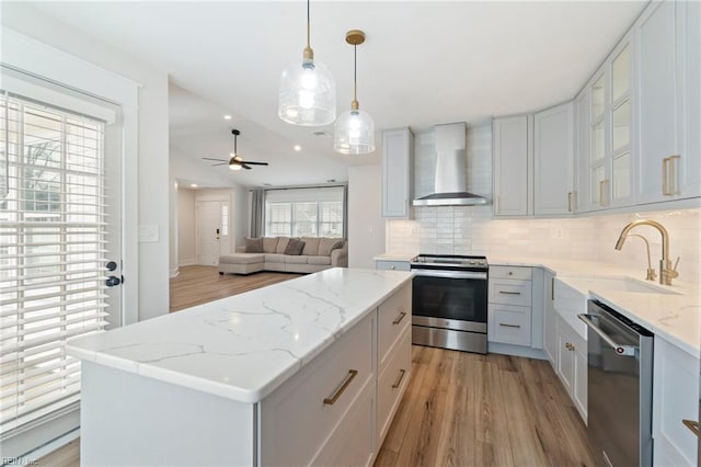 kitchen featuring a center island, stainless steel appliances, decorative backsplash, a sink, and wall chimney range hood