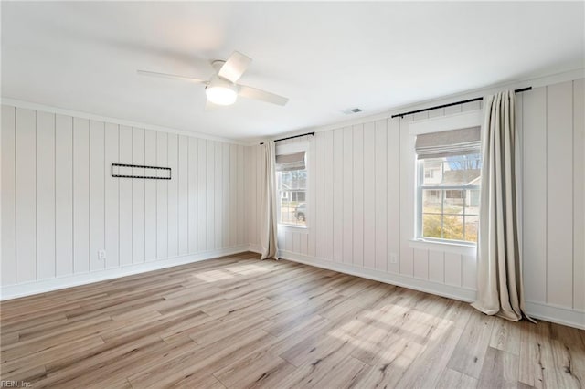 empty room featuring light wood finished floors, plenty of natural light, visible vents, and a ceiling fan