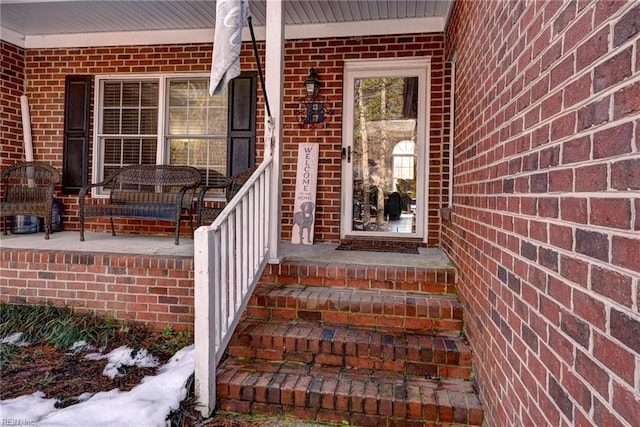 snow covered property entrance featuring covered porch and brick siding