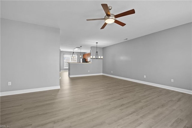 unfurnished living room with wood finished floors, baseboards, and ceiling fan with notable chandelier