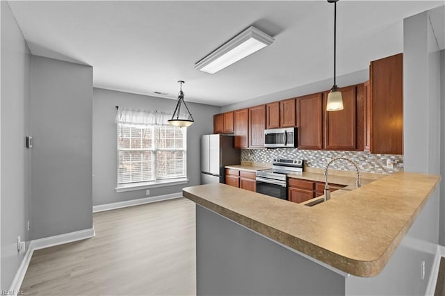 kitchen with appliances with stainless steel finishes, pendant lighting, brown cabinets, and a peninsula