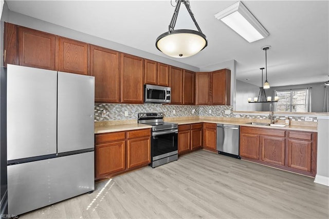 kitchen featuring a sink, light countertops, appliances with stainless steel finishes, brown cabinetry, and pendant lighting