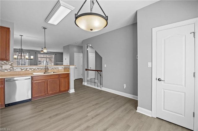 kitchen featuring brown cabinets, decorative light fixtures, light countertops, a sink, and dishwasher