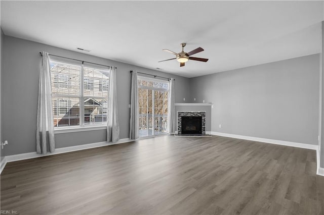 unfurnished living room with ceiling fan, dark wood-type flooring, a fireplace, visible vents, and baseboards