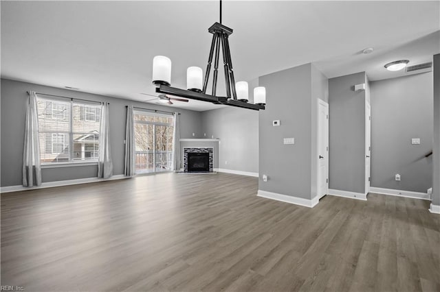 unfurnished living room with a fireplace, wood finished floors, visible vents, a ceiling fan, and baseboards