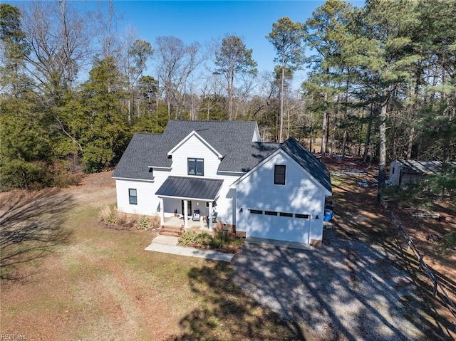 view of front of home with gravel driveway, roof with shingles, covered porch, metal roof, and a garage