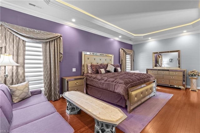 bedroom featuring hardwood / wood-style flooring, visible vents, ornamental molding, multiple windows, and a raised ceiling