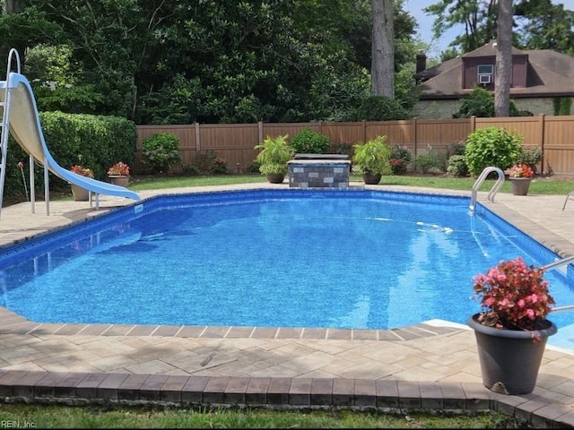 view of swimming pool with a fenced backyard, a fenced in pool, a water slide, and a patio