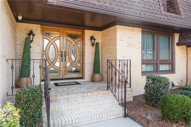 view of exterior entry featuring a shingled roof, french doors, brick siding, and a porch