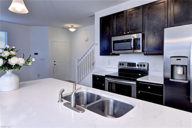 kitchen featuring dark brown cabinetry, light stone countertops, stainless steel appliances, pendant lighting, and a sink