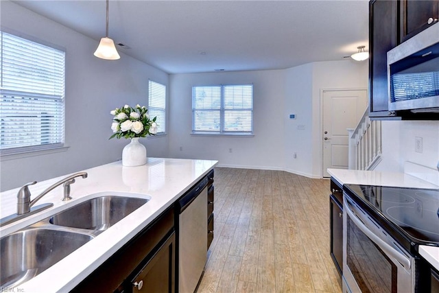 kitchen featuring pendant lighting, stainless steel appliances, light countertops, a sink, and light wood-type flooring