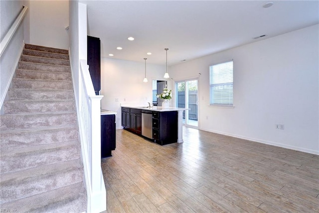 kitchen with pendant lighting, a center island with sink, light countertops, light wood-style flooring, and stainless steel dishwasher