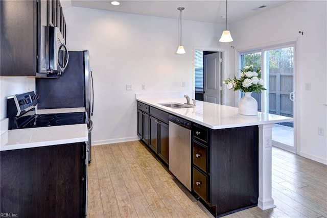 kitchen with pendant lighting, stainless steel appliances, light countertops, light wood-style flooring, and a sink