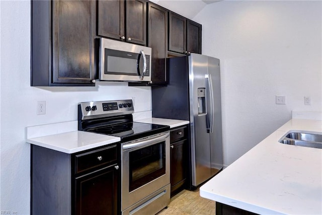 kitchen with light wood finished floors, appliances with stainless steel finishes, light countertops, dark brown cabinets, and a sink