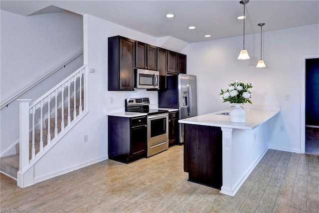 kitchen with light wood finished floors, stainless steel appliances, light countertops, hanging light fixtures, and dark brown cabinets