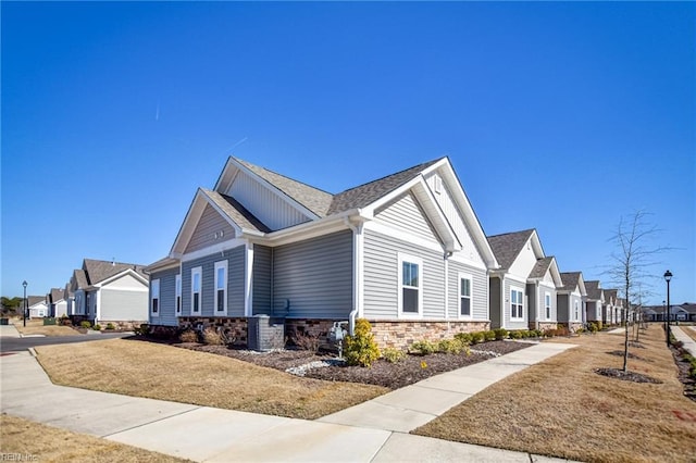 view of side of property featuring stone siding, a residential view, board and batten siding, and roof with shingles