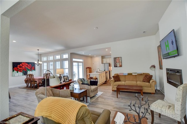 living area with baseboards, recessed lighting, light wood-style flooring, and an inviting chandelier