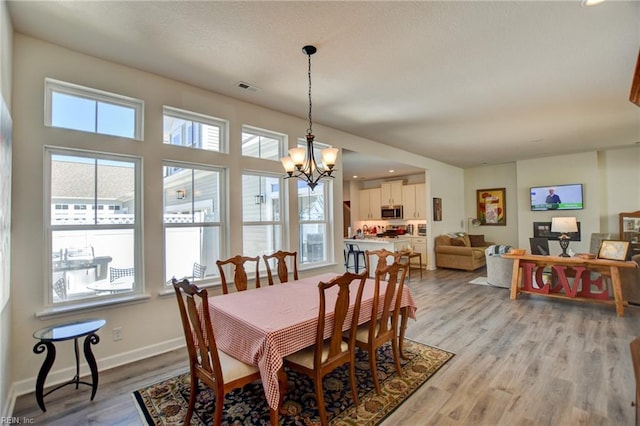 dining area with a notable chandelier, light wood-style flooring, visible vents, and baseboards