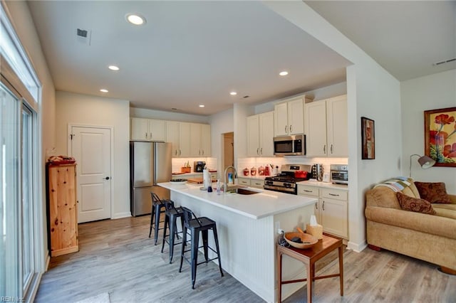 kitchen with light wood finished floors, appliances with stainless steel finishes, visible vents, and a breakfast bar