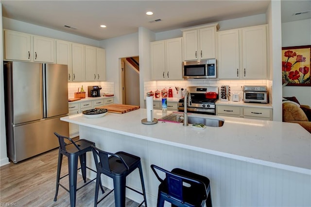 kitchen featuring light wood finished floors, backsplash, stainless steel appliances, light countertops, and a sink