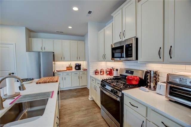 kitchen featuring decorative backsplash, appliances with stainless steel finishes, light countertops, light wood-type flooring, and a sink