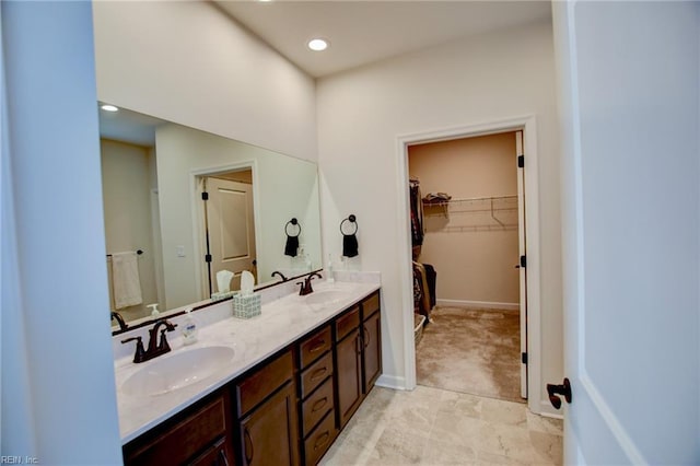 bathroom featuring double vanity, a spacious closet, baseboards, and a sink