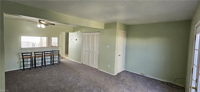 empty room with baseboards, dark carpet, and a ceiling fan