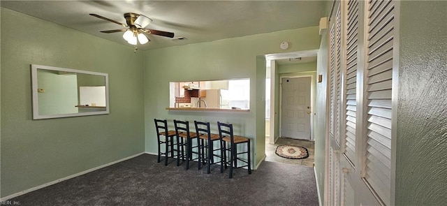 interior space with baseboards, visible vents, a ceiling fan, freestanding refrigerator, and dark carpet