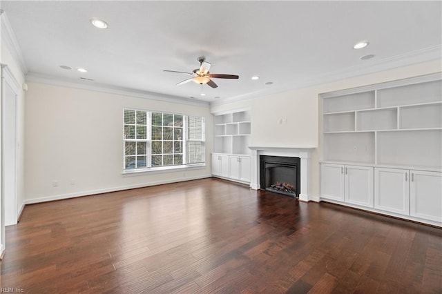 unfurnished living room featuring a ceiling fan, ornamental molding, dark wood-type flooring, a lit fireplace, and built in shelves